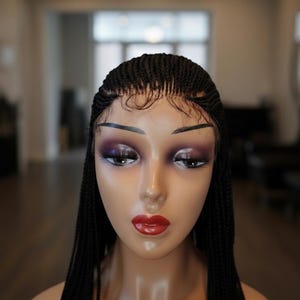 Peut inclure: Tête de mannequin avec une perruque tressée noire. La perruque présente un devant en dentelle et de longues tresses fluides. Le mannequin est entièrement maquillé, avec de l'ombre à paupières foncée et du rouge à lèvres rouge.