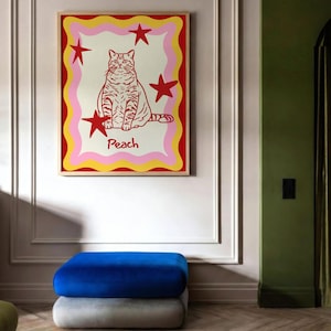May include: A framed art print featuring a stylized cat illustration. The cat is red with stripes, surrounded by red stars and a wavy border of pink, yellow, and red. The word "Peach" is below the cat.