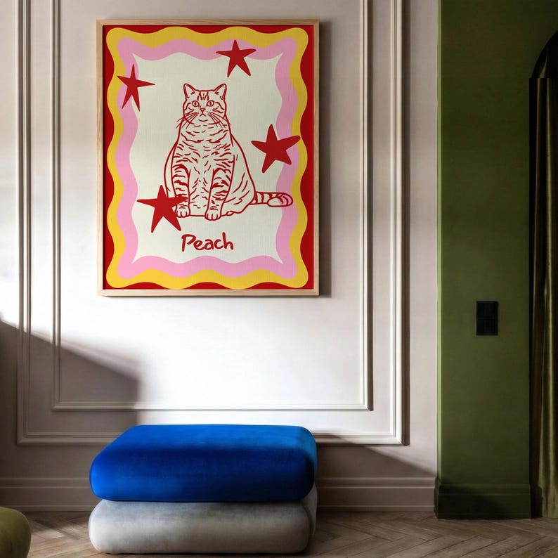 May include: A framed art print featuring a stylized cat illustration. The cat is red with stripes, surrounded by red stars and a wavy border of pink, yellow, and red. The word "Peach" is below the cat.