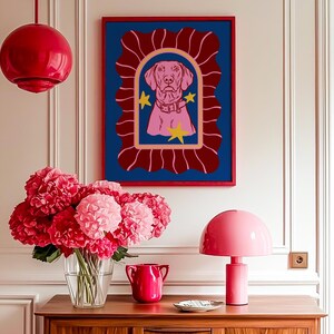 May include: A framed dog portrait in a red frame with a blue background and a pink dog illustration. The room features a pink lamp, a vase of pink flowers, and a red pendant light.