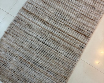 Peut inclure: Tapis rectangulaire avec un motif rayé texturé. Le tapis présente un mélange de couleurs neutres, notamment beige, marron et blanc cassé, créant une esthétique naturelle et terreuse. Les fibres sont disposées en lignes parallèles.