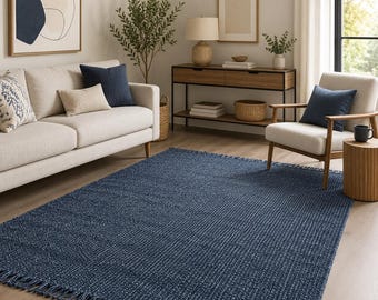 Può includere: Un tappeto rettangolare di colore blu navy intenso con una trama spessa e testurizzata, caratterizzato da frange sui bordi corti. Il tappeto è posizionato su un pavimento in legno chiaro in una stanza arredata con mobili dai toni neutri.