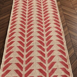 An overhead view of a long runner rug with a red and cream herringbone pattern on a dark wood floor.