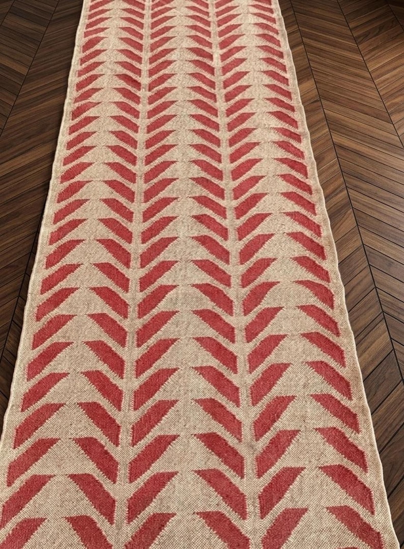 An overhead view of a long runner rug with a red and cream herringbone pattern on a dark wood floor.