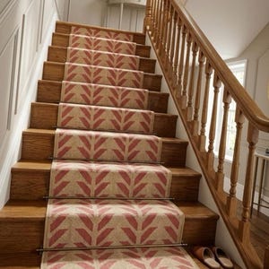 A red and cream herringbone pattern runner rug on wooden stairs with a light wood banister and white wainscoting.