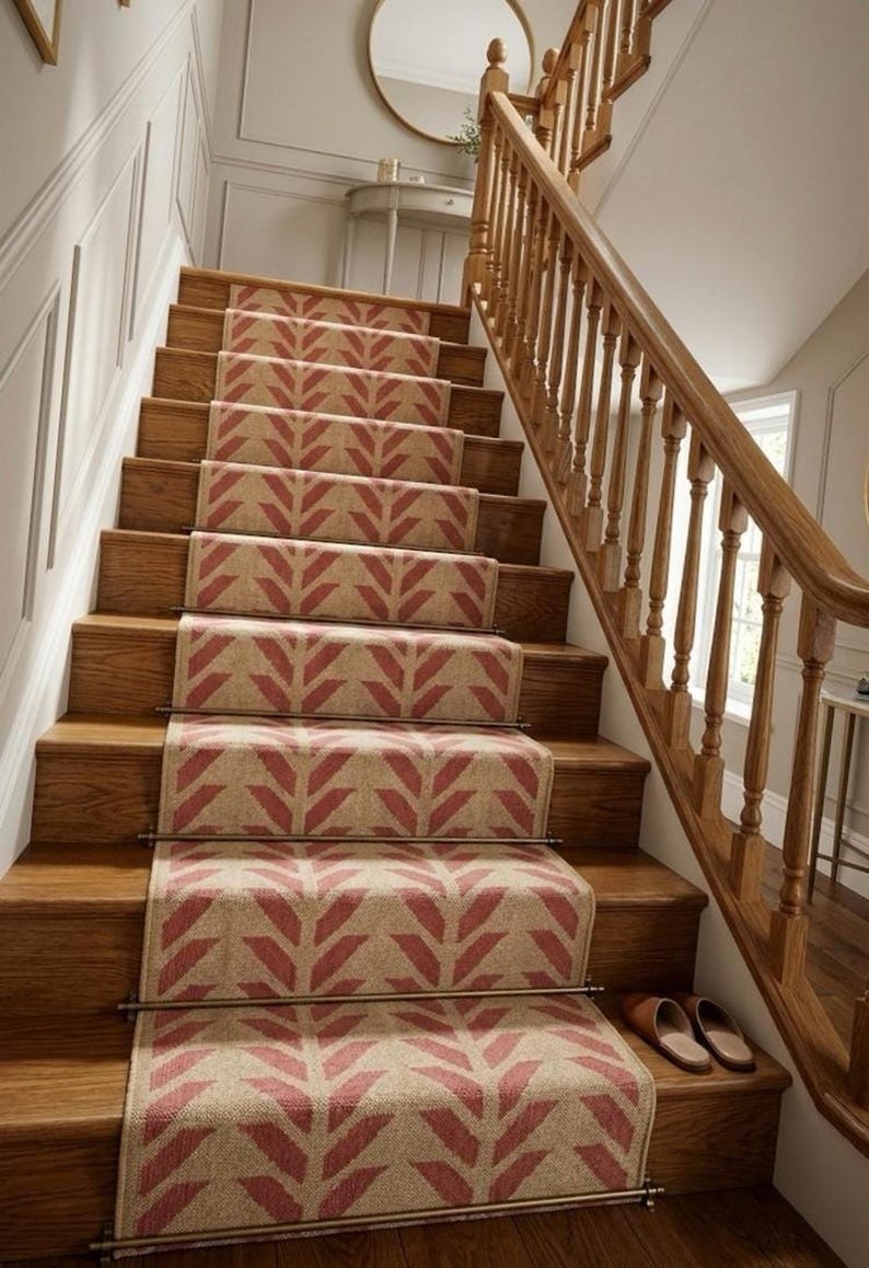 A red and cream herringbone pattern runner rug on wooden stairs with a light wood banister and white wainscoting.