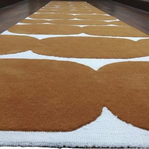 A close-up, low-angle view of a mustard yellow and white geometric runner rug with wavy shapes on a dark wood floor.