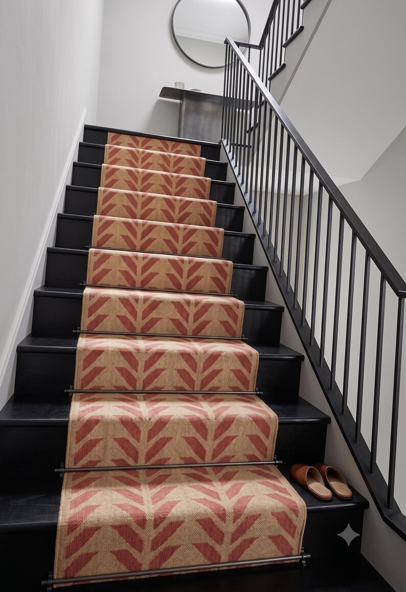 A red and cream herringbone pattern runner rug on black painted stairs with a black metal banister, with two brown slippers at the bottom.