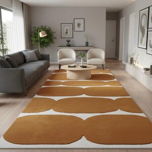 A mustard yellow and white geometric runner rug with wavy shapes on a light wood floor in a living room with a gray sofa and two cream armchairs.