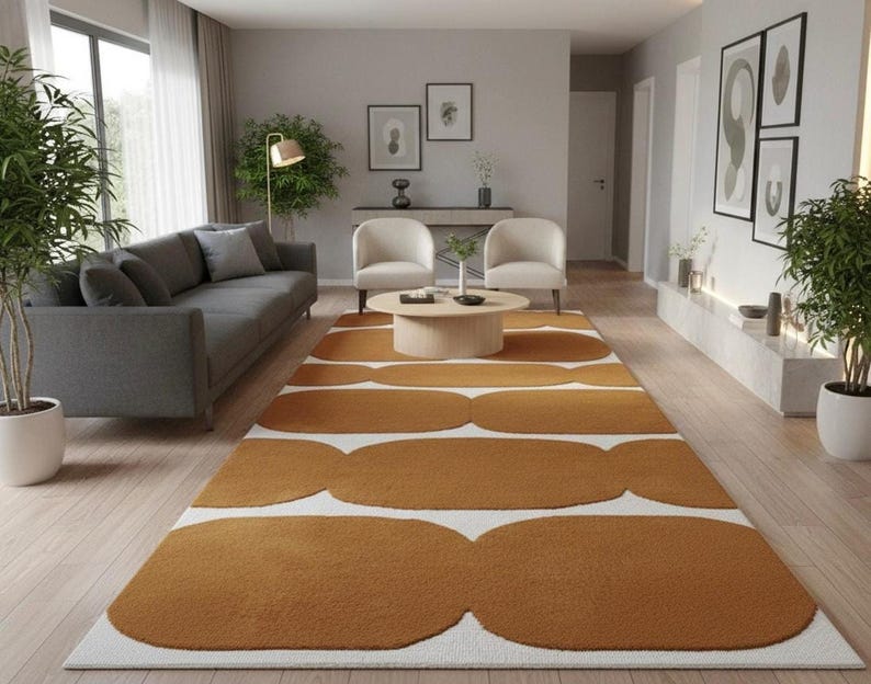 A mustard yellow and white geometric runner rug with wavy shapes on a light wood floor in a living room with a gray sofa and two cream armchairs.