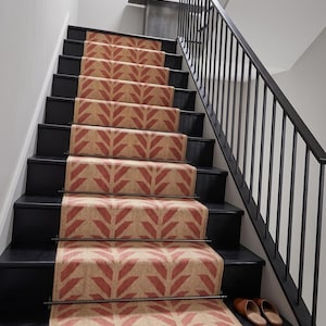 A red and cream herringbone pattern runner rug on black painted stairs with a black metal banister and white walls.