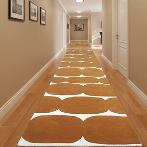 A long mustard yellow and white geometric runner rug with wavy shapes extends down a narrow hallway with light brown walls and recessed lighting.