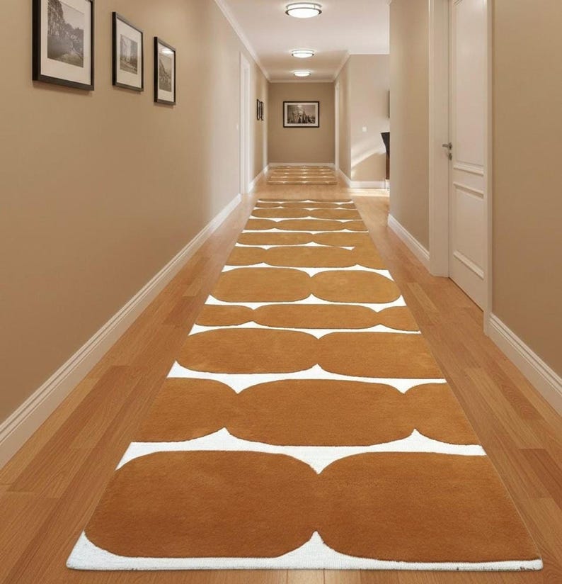 A long mustard yellow and white geometric runner rug with wavy shapes extends down a narrow hallway with light brown walls and recessed lighting.