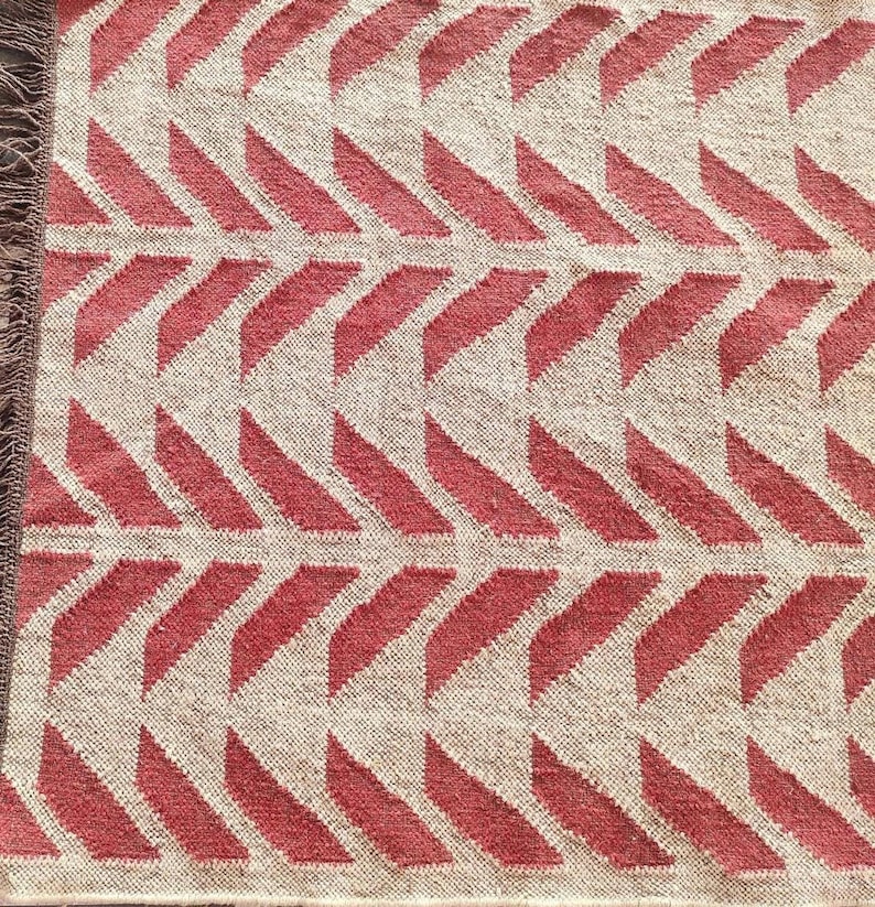 A close-up, overhead view of a red and cream herringbone pattern rug with visible fringe on the left edge.