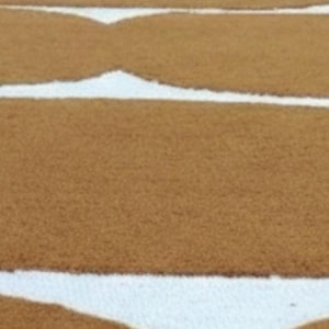 An overhead, slightly blurry view of multiple mustard yellow and white wavy geometric rugs laid out in rows on a dark surface.