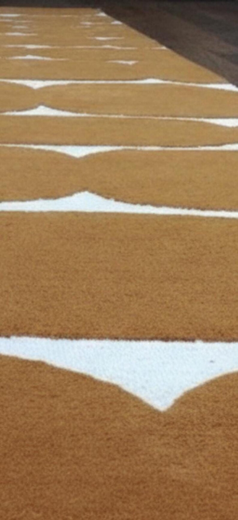 An overhead, slightly blurry view of multiple mustard yellow and white wavy geometric rugs laid out in rows on a dark surface.