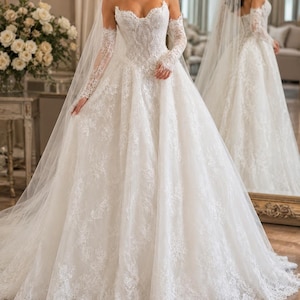 May include: A white strapless ball gown wedding dress featuring an intricate lace bodice and a full, floor-length skirt with lace appliques. The dress includes matching sheer lace long sleeves and a long, flowing veil that drapes over the shoulders.