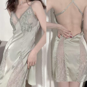 May include: Sage green satin slip dress with delicate lace detailing. The dress features a V-neckline with lace accents and a low back design. The lace is visible on the bodice and along the skirt's sides, creating a romantic and elegant look.