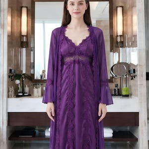 May include: A purple lingerie set featuring a long, sheer robe with bell sleeves and a matching slip dress. The dress and robe are adorned with intricate lace detailing. The set is designed for sleepwear and loungewear.