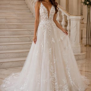 May include: A floor-length A-line gown in an off-white shade featuring a deep V-neckline and thin straps. The bodice and skirt are adorned with intricate white leaf-shaped lace appliqu&eacute;s that cascade down the layered tulle fabric to the hem.