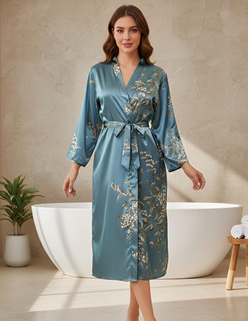 May include: A teal satin robe with a floral pattern and a matching belt. The robe has long sleeves and a V-neck. The floral design features white and gold accents. The robe is knee-length and appears to be made of a silky material.