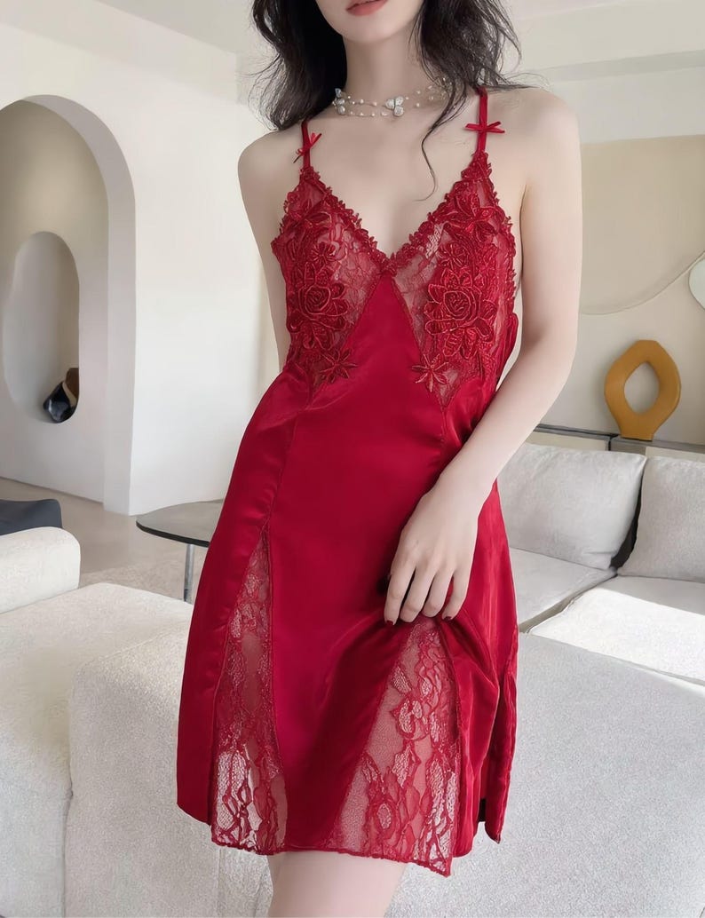 May include: A red satin slip dress with delicate lace detailing. The dress features a V-neckline with floral lace accents and thin straps with small bows. Lace panels adorn the sides of the dress, adding a touch of elegance. A stylish and comfortable nightgown.