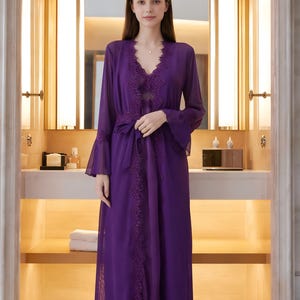 May include: A long, flowing purple robe with lace trim and bell sleeves. The robe is tied at the waist with a matching sash. The neckline is a V-shape, and the fabric appears to be sheer. The robe is worn over a matching slip.