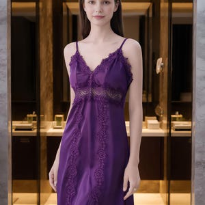 May include: A long, purple satin nightgown with delicate lace trim along the neckline and bodice. The dress features thin spaghetti straps and decorative lace detailing down the front. The nightgown is a deep shade of purple.