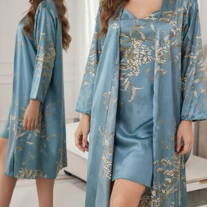 May include: A light blue satin pajama set featuring a floral pattern in gold and white. The set includes a slip dress and a long-sleeved robe. The robe has a shawl collar and is open in the front. The dress has a V-neck.