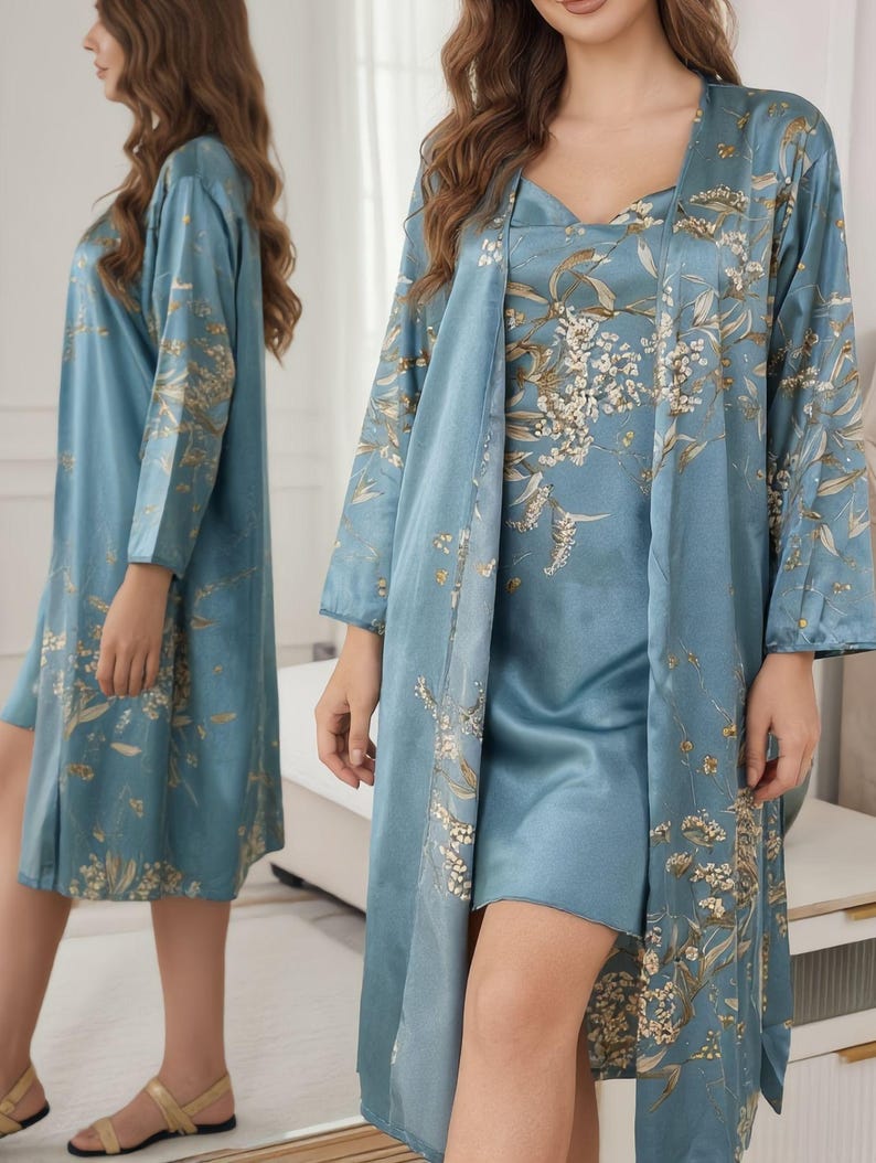 May include: A light blue satin pajama set featuring a floral pattern in gold and white. The set includes a slip dress and a long-sleeved robe. The robe has a shawl collar and is open in the front. The dress has a V-neck.