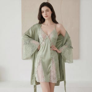 May include: Sage green satin lingerie set featuring a slip dress with lace detailing and a matching robe. The slip dress has a V-neckline and lace inserts. The robe has wide sleeves with lace trim. A delicate and elegant sleepwear ensemble.