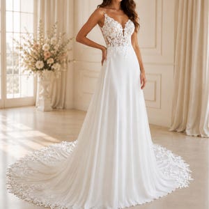 May include: A floor-length white gown featuring a sleeveless bodice with intricate floral lace applique, a deep V-neckline, and thin spaghetti straps. The skirt is made of flowing fabric that extends into a long, lace-trimmed circular train.