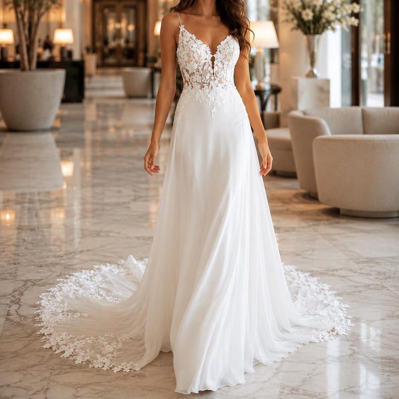 May include: A floor-length white wedding dress featuring a sleeveless bodice with intricate floral lace appliques, a deep V-neckline, and a flowing skirt that transitions into a lace-trimmed train. The design includes thin straps and a fitted waist.