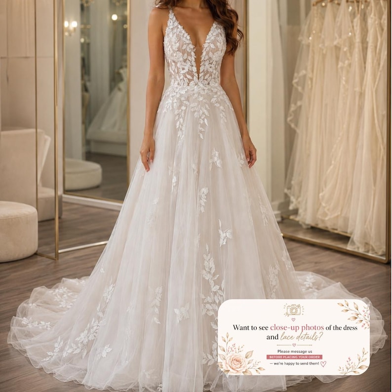 May include: A floor-length white gown featuring a deep V-neckline and thin straps. The bodice and skirt are adorned with white floral lace appliqu&eacute;s that cascade down the tulle fabric. The text reads: Want to see close-up photos of the dress and lace details? Please message us before placing your order.