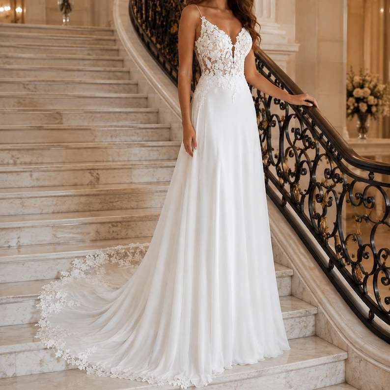 May include: A floor-length white gown featuring a sleeveless bodice with intricate floral lace appliques, a deep V-neckline, and a flowing skirt that extends into a long train with a scalloped lace hemline detail along the bottom edge.