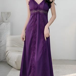 May include: A long, purple slip dress with delicate spaghetti straps and a V-neckline. The dress features intricate lace detailing along the bodice and down the front, creating a romantic and elegant look. The dress is made of a smooth, flowing fabric.