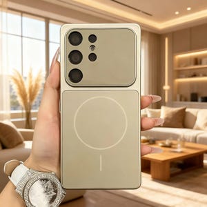 Könnte beinhalten: Eine goldfarbene Handyhülle mit rechteckigem Design. Die Hülle hat ein Kameramodul mit mehreren Linsen und einen unteren Bereich mit kreisförmigem Design. Die Hülle wird in einer Hand gehalten, und eine Uhr mit weißem Armband und silbernem Zifferblatt ist sichtbar.