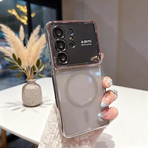 Może przedstawiać: Przezroczyste etui na telefon ze srebrną ramką i szarym tyłem. Etui posiada czarny moduł aparatu z napisem "4K 120 FPS". Etui ma chronić telefon przed zarysowaniami i uszkodzeniami.