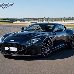 May include: A dark blue Aston Martin DBS I sports car on a racetrack. The car has a sleek, aerodynamic design with black wheels and a prominent front grille. The Aston Martin logo is visible above the car.