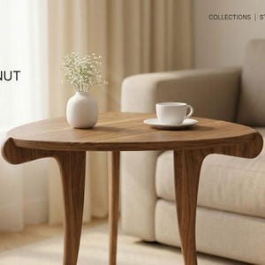 May include: A wooden side table with a triangular top and three curved legs. A white vase with small white flowers and a white teacup and saucer sit on the table. The text "AURA & WALNUT" is displayed in the upper left corner.