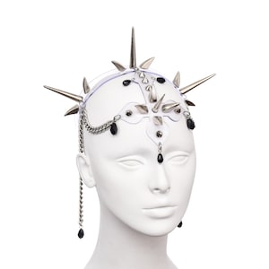 May include: A silver spiked headpiece with black beads hanging from chains. The headpiece is worn on a white mannequin head.