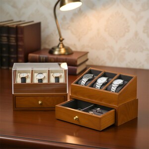 May include: Wooden watch display cases with drawers. One case has a clear top and holds three watches. The other case has an open top and holds three watches. Both cases are made of wood and have a drawer with a gold knob.