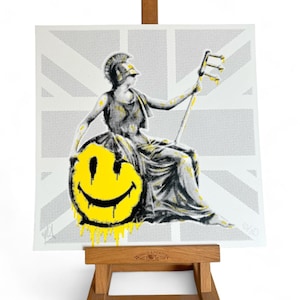 May include: A print on canvas of a classical figure playing a stringed instrument, with a large yellow smiley face. The background features a gray and white Union Jack design. The artwork is displayed on a wooden easel.