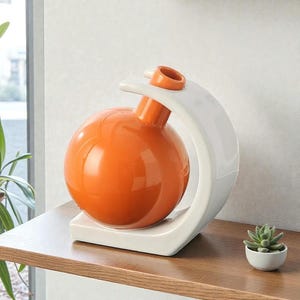 Peut inclure: Un vase en céramique orange moderne avec un corps sphérique et un support blanc incurvé. Le vase a une petite ouverture en haut et repose sur une base blanche. Une petite plante succulente dans un pot blanc est à côté du vase.