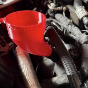 May include: A bright red plastic funnel with a curved neck inserted into a vehicle engine bay. The funnel features the embossed text 228PRINTSHOP on its side. It is positioned among various black rubber hoses, metallic components, and engine parts.