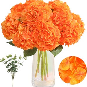 May include: A bouquet of vibrant orange artificial hydrangeas in a clear glass vase. The flowers have multiple layers of petals and green leaves. A sprig of green eucalyptus is to the left, and a close-up of the petals is in the lower right.