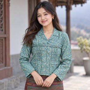 May include: A long-sleeved teal jacket featuring a small-scale floral pattern in yellow and white. The garment includes a collared neckline, a horizontal pleated panel across the chest, and two front pockets. It is paired with a striped skirt.