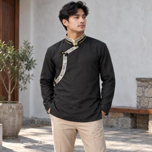 May include: A black long-sleeved shirt with a mandarin collar and an asymmetrical front placket featuring a grey patterned trim with yellow piping and black knot buttons, paired with light beige trousers.