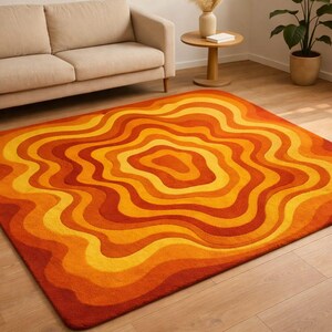 May include: A rectangular rug with a retro design. The rug features concentric wavy lines in shades of orange, yellow, and red. The rug is placed on a wooden floor, with a beige sofa in the background.
