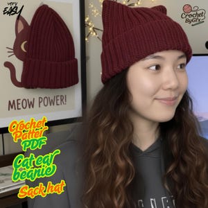 Può includere: Un berretto bordeaux con orecchie da gatto in tessuto a coste. Il cappello ha due orecchie a punta sulla parte superiore. Le parole "very easy" sono nell'angolo in alto a sinistra. Le parole "MEOW POWER!" sono sotto un'illustrazione di gatto.